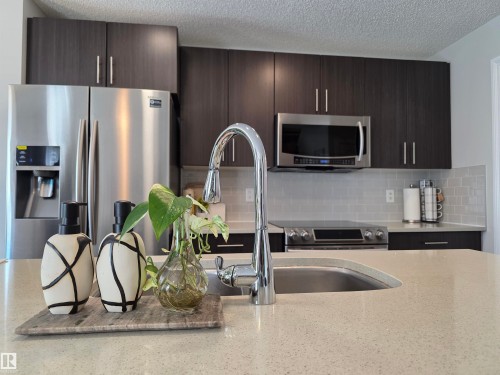Kitchen featuring dark wood-finish cabinetry, stainless steel appliances, light-toned countertop, and subway tile backsplash - 491 Ebbers Way, Edmonton, AB 