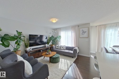 Bright living area featuring wood-finish flooring, a contemporary ceiling light fixture, and white window treatments - 491 Ebbers Way, Edmonton, AB 
