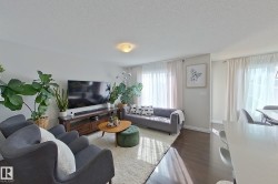 Bright living area featuring wood-finish flooring, a contemporary ceiling light fixture, and white window treatments - 