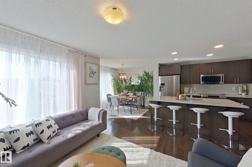 Open-concept living space featuring wood-finish flooring, recessed lighting, a kitchen island with seating, a stainless steel appliance suite, and light-toned walls - 491 Ebbers Way, Edmonton, AB 