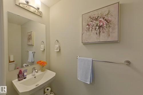 Pedestal sink with chrome faucet, large wall-mounted mirror, and brushed nickel light fixture - 491 Ebbers Way, Edmonton, AB 