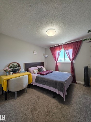 Bedroom featuring a wood-finish headboard, textured carpeting, and a window with natural light - 491 Ebbers Way, Edmonton, AB 