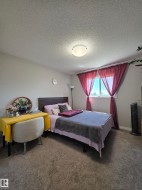 Bedroom featuring a wood-finish headboard, textured carpeting, and a window with natural light - 