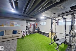 Versatile lower-level space featuring a turf-style flooring, painted exposed ceiling joists, recessed lighting, and wall-mounted shelving - 