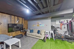 Recreation room featuring wood-finish accent wall, exposed ceiling joists, and a mix of carpet and artificial turf flooring - 