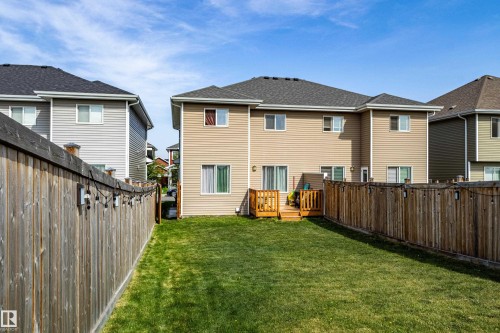 Expansive grass yard bordered by a privacy fence, featuring a raised wood deck with railings, and a tan siding exterior with multiple windows and sliding patio doors - 491 Ebbers Way, Edmonton, AB 