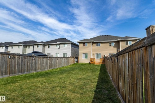 Spacious backyard featuring a manicured lawn, a wooden privacy fence with string lights, and a rear deck with wooden railings - 491 Ebbers Way, Edmonton, AB 