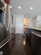 Kitchen featuring wood-finish flooring, stainless steel appliances, dark cabinetry, light countertops, and recessed lighting - 
