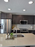 Kitchen featuring a stainless steel undermount sink, a chrome gooseneck faucet, light-toned countertops, dark wood-finish cabinetry, and a light-toned subway tile backsplash - 