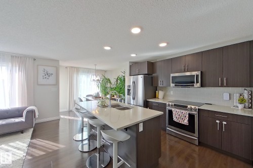 Modern kitchen featuring dark wood-finish cabinetry, stainless steel appliances, and a light-toned countertop - 491 Ebbers Way, Edmonton, AB 