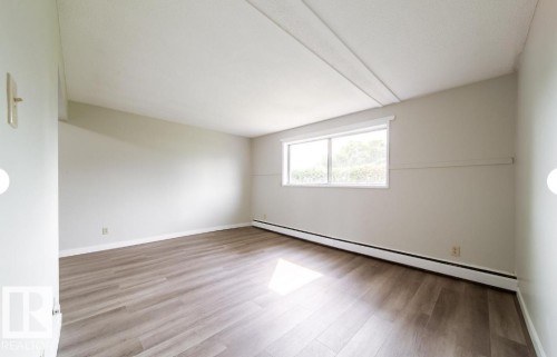 Spacious room featuring wood-finish flooring, light-toned wall paint, a large window, and baseboard heating - 3415 106 Avenue Northwest, Edmonton, AB - Indoor Photo Showing Other Room