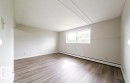 Spacious room featuring wood-finish flooring, light-toned wall paint, a large window, and baseboard heating - 3415 106 Avenue Northwest, Edmonton, AB  - Indoor Photo Showing Other Room 