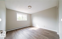 Spacious room featuring wood-finish flooring, a large window, neutral wall tones, baseboard heating, and a flush-mount ceiling light fixture - 