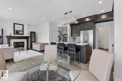 Open-concept living area featuring wood-finish flooring, a stone-faced fireplace with a dark wood mantel, and a kitchen island with seating - 