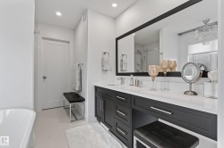 Spacious bathroom featuring a dual vanity with dark cabinetry and light countertops, an integrated makeup area, a large wall-mounted mirror, and recessed lighting - 