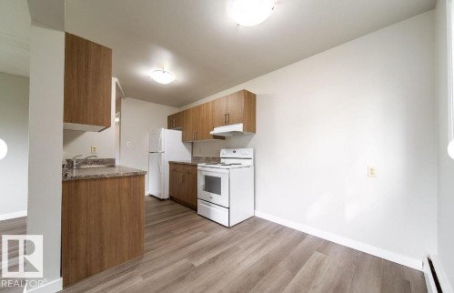Kitchen featuring wood-finish cabinetry, stone-look countertops, and white appliances - 3415 106 Avenue Northwest, Edmonton, AB - Indoor Photo Showing Kitchen