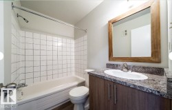 Bathroom featuring a white bathtub, tiled shower surround, wood-finish vanity with an integrated sink, stone-look countertop, and a wood-framed mirror - 