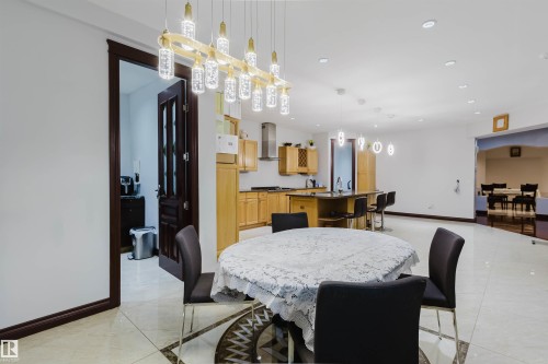 Open-concept interior featuring light-toned large format tile flooring, a dining area with a modern linear chandelier, and a kitchen with light wood cabinetry and a dark countertop - 4103 Westcliff Heath Heath Sw, Edmonton, AB - Indoor Photo Showing Dining Room