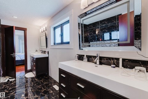Contemporary bathroom featuring dual dark wood-finish vanities with integrated white sinks, black marble-patterned floor tiling, an illuminated vanity mirror, and recessed ceiling lighting - 4103 Westcliff Heath Heath Sw, Edmonton, AB - Indoor Photo Showing Bathroom