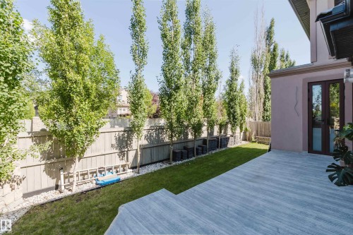 Spacious outdoor deck featuring light-toned wood-finish flooring, bordered by a manicured lawn and a row of mature columnar trees - 4103 Westcliff Heath Heath Sw, Edmonton, AB - Outdoor