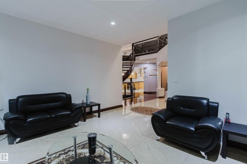 Spacious living area featuring light-toned flooring, recessed lighting, and a prominent dark wood spiral staircase with glass and metal railings - 4103 Westcliff Heath Heath Sw, Edmonton, AB - Indoor