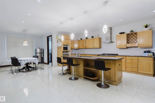 Spacious kitchen featuring light wood cabinetry, a central island with integrated seating, and a stainless steel range hood - 4103 Westcliff Heath Heath Sw, Edmonton, AB - Indoor