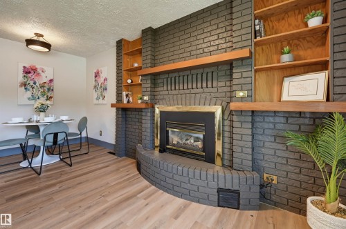 Brick fireplace with a brass-trimmed insert, wood-finish flooring, built-in shelving, and a recessed ceiling light fixture - 8716 130 Avenue Nw, Edmonton, AB - Indoor Photo Showing Living Room With Fireplace