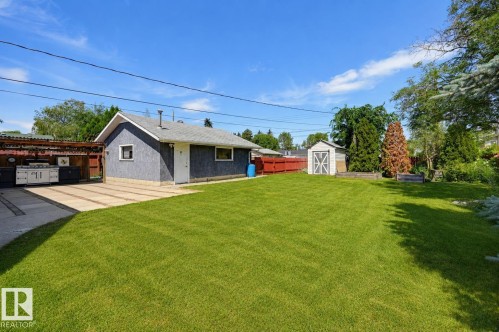 Expansive lawn area featuring a concrete patio with an outdoor kitchen setup, a storage shed, and mature perimeter trees - 8716 130 Avenue Nw, Edmonton, AB - Outdoor