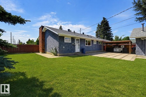 Spacious backyard featuring a manicured lawn, brick chimney, and a covered outdoor entertaining area - 8716 130 Avenue Nw, Edmonton, AB - Outdoor