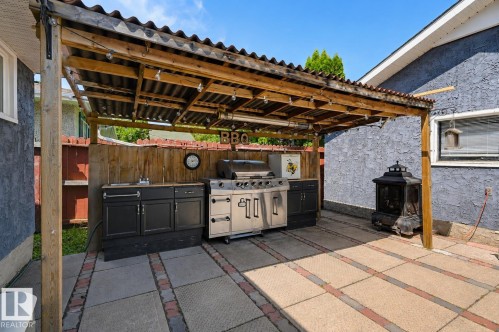 Outdoor kitchen featuring a corrugated roof pergola, integrated sink, built-in cabinetry, and paver patio with brick accents - 8716 130 Avenue Nw, Edmonton, AB - Outdoor