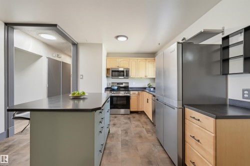 Kitchen featuring an expansive island with storage, stainless steel appliances, wood-finish flooring, light wood cabinetry, and dark countertops - 8716 130 Avenue Nw, Edmonton, AB - Indoor Photo Showing Kitchen With Stainless Steel Kitchen