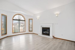 Spacious living area featuring an arched window, light wood-finish flooring, a white mantel fireplace, and two wall sconces - 