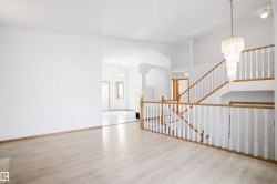 Open-concept interior featuring light wood-finish flooring, a grand staircase with white balusters and wood handrails, a tiered chandelier, and arched doorways - 