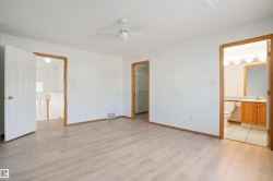 Spacious room featuring light wood-finish flooring, white walls, and a ceiling fan - 