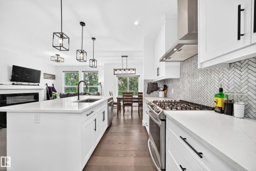 Contemporary kitchen featuring a large center island with integrated sink, white cabinetry with matte black hardware, stainless steel gas range, and a herringbone pattern tile backsplash - 22270 99A Avenue Nw, Edmonton, AB - Indoor Photo Showing Kitchen With Upgraded Kitchen