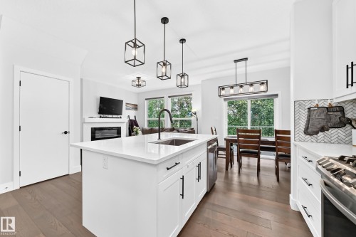 Open-concept kitchen featuring a large island with a sink, white cabinetry with matte black hardware, and wood-finish flooring - 22270 99A Avenue Nw, Edmonton, AB - Indoor Photo Showing Kitchen With Upgraded Kitchen