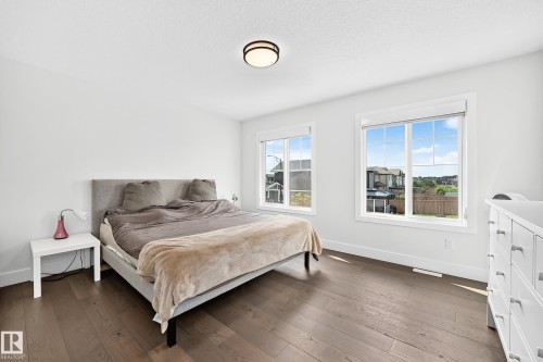 Spacious bedroom featuring dark wood-finish flooring, two large windows with white trim, and a contemporary ceiling light fixture - 22270 99A Avenue Nw, Edmonton, AB - Indoor Photo Showing Bedroom