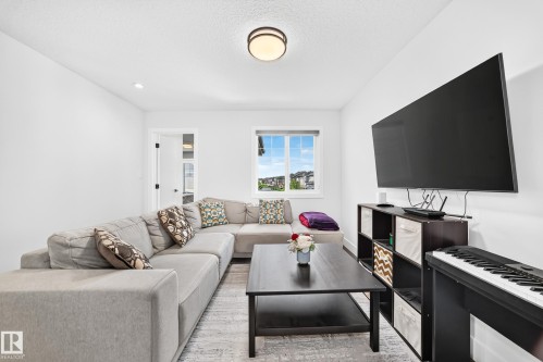 Bright room with white painted walls and ceiling, featuring a flush-mount ceiling light fixture, a large window, and a dark wood-finish media console - 22270 99A Avenue Nw, Edmonton, AB - Indoor Photo Showing Living Room