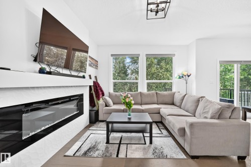 Modern living area featuring a linear electric fireplace with textured white tiling, a wood-finish flooring, and multiple large windows with natural light - 22270 99A Avenue Nw, Edmonton, AB - Indoor Photo Showing Living Room With Fireplace