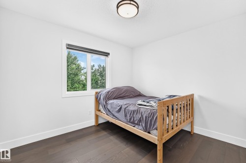 Bright room featuring a window with a roller shade, dark wood-finish flooring, white baseboards, and a flush-mount ceiling light - 22270 99A Avenue Nw, Edmonton, AB - Indoor Photo Showing Bedroom