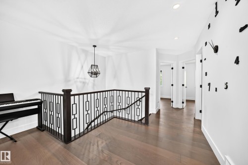 Hardwood flooring extends throughout this upper-level landing, featuring a dark wood newel post and balusters with geometric metal infill panels - 22270 99A Avenue Nw, Edmonton, AB - Indoor Photo Showing Other Room