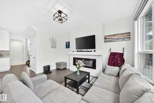 Living area featuring a contemporary linear fireplace with a textured tile surround, dark wood-finish flooring, and crisp white walls - 22270 99A Avenue Nw, Edmonton, AB - Indoor Photo Showing Living Room With Fireplace