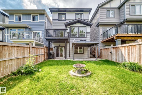 Expansive backyard featuring a manicured lawn, full fencing, an upper-level deck with black railing, a ground-level covered patio, and a lower-level glass sliding door entry - 22270 99A Avenue Nw, Edmonton, AB - Outdoor