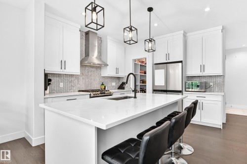 Modern kitchen featuring a white quartz-topped island with a black matte faucet, white shaker-style cabinetry, stainless steel appliances, and dark wood-finish flooring - 22270 99A Avenue Nw, Edmonton, AB - Indoor Photo Showing Kitchen With Upgraded Kitchen