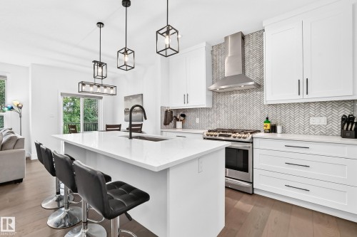 Contemporary kitchen featuring an island with a built-in sink, white cabinetry with black hardware, stainless steel appliances, a herringbone tile backsplash, and wood-finish flooring - 22270 99A Avenue Nw, Edmonton, AB - Indoor Photo Showing Kitchen With Upgraded Kitchen