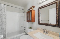 Bathroom featuring a white bathtub with shower, wall-mounted showerhead, and a vanity with a light-toned countertop - 