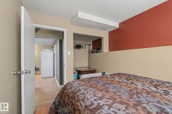 Bedroom featuring wood-finish flooring, two-tone wall paint, and an open doorway leading to an additional space with a built-in refrigerator - 