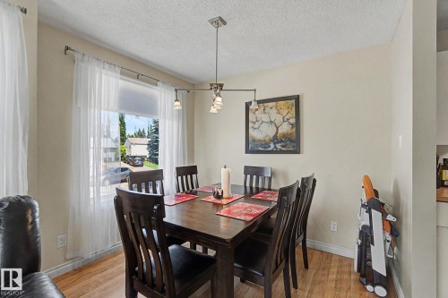 Dining area featuring wood-finish flooring, a large window with sheer curtains, and a contemporary ceiling light fixture - 64 Pipestone, Devon, AB - Indoor Photo Showing Dining Room