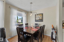 Dining area featuring wood-finish flooring, a large window with sheer curtains, and a contemporary ceiling light fixture - 