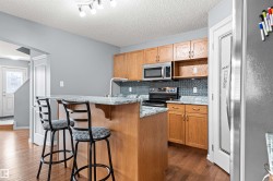 Kitchen featuring wood-finish cabinetry, granite-style countertops, mosaic tile backsplash, stainless steel appliances, and a central island with an integrated breakfast bar - 